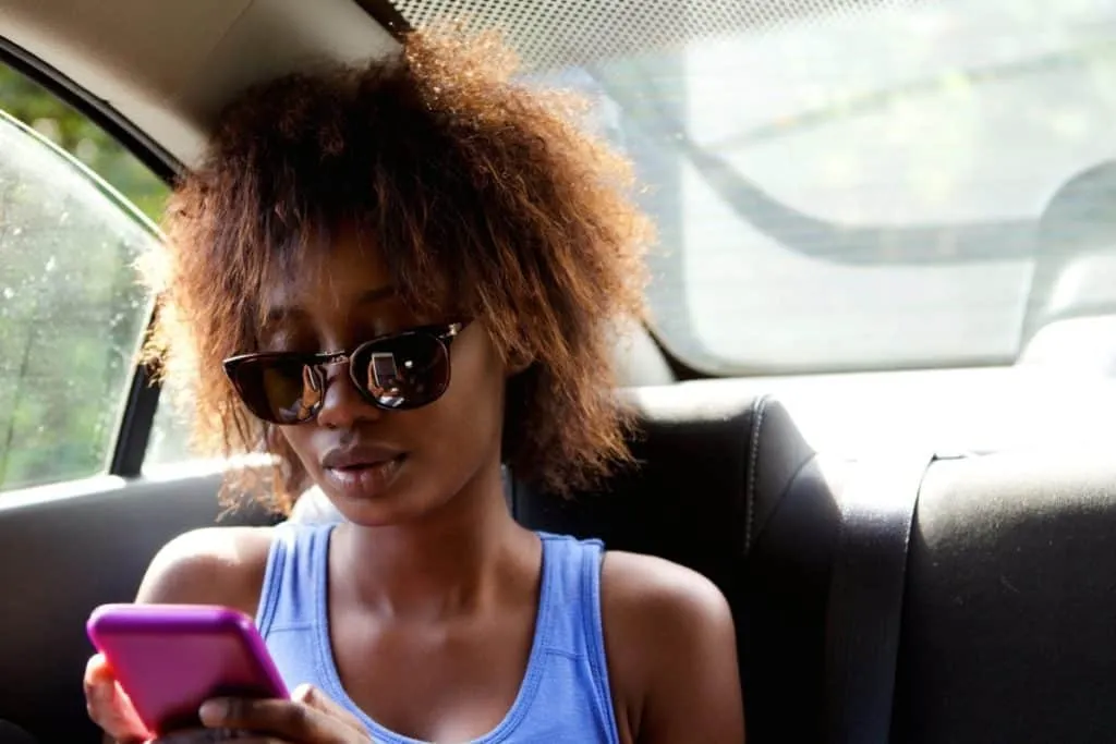 Close up portrait of a young african american woman sitting n backseat of car looking at cell phone